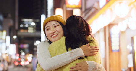 Woman, friends and hug in Japanese city or happy reunion for party night, adventure or Tokyo. Female people, embrace and dark or bokeh on street with light or international travel, journey or eveningの写真素材
