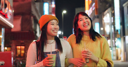 Night, travel and Japanese women in a city walking, talking and bonding with milkshake drink outdoor. Happy, female and friends in Japan with bubble tea boba, conversation and fun evening adventureの写真素材