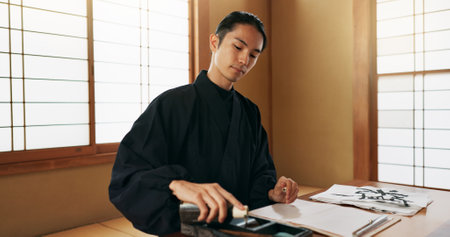 Black ink, Asian man or Japanese artist in studio for art and script, calligraphy with paper for alphabet. Start, ready or creative person with tools, paintbrush and focus with traditional stationeryの写真素材