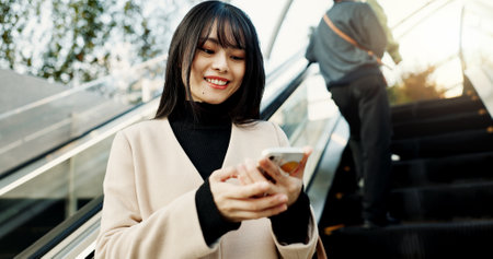 Phone, smile and a Japanese woman on escalator in city, social media app or reading email notification in Tokyo. Smartphone, mobile or happy person in urban street outdoor on communication technologyの写真素材