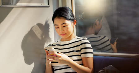 Asian woman, train and travel with smartphone and communication, commute or adventure with transport. Email, chat and scroll social media with tourism in Japan, public transportation and mobile appの写真素材