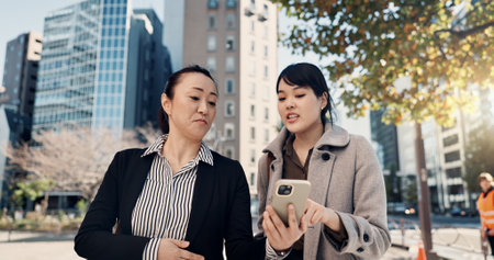 Phone, city and Japanese business woman walking to work together for travel, journey or commute. Collaboration, planning and discussion with employee team reading text message outdoor in Tokyoの写真素材