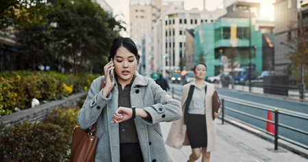 Phone call, watch and Japanese businesswoman in city, late for work on Tokyo street or sidewalk. Stress, time and schedule with young professional employee walking on road in rush for appointmentの写真素材