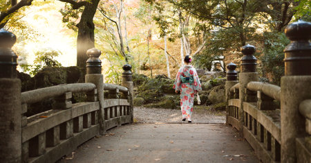 Bridge, walking and Japanese woman in park for wellness, fresh air and relaxing in nature. Travel, traditional and person in indigenous clothes, fashion and kimono outdoors for zen, calm and peaceの写真素材