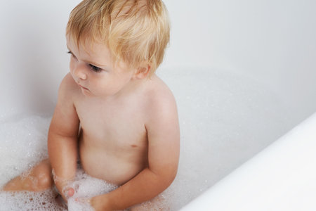 Baby in bath, clean with bubbles and soap for morning routine with health, wellness and body care in home. Cute toddler washing in foam with hygiene, relax and calm child sitting in water in bathroomの写真素材