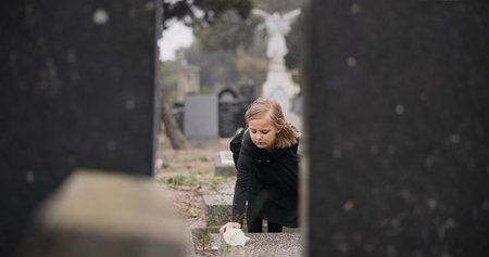 Flower, death or kid in cemetery for funeral. spiritual service or tombstone for respect in Christian religion. Mourning, sad or depressed girl child outside in graveyard for grief, loss or farewellの写真素材