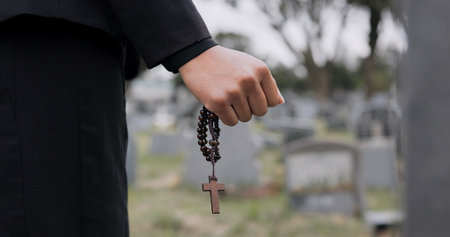 Rosary, death or hand cemetery for funeral. spiritual service or grave visit to repsect the Christian religion. Mourning, goodbye or closeup of person outside in graveyard for grief, loss or farewellの写真素材