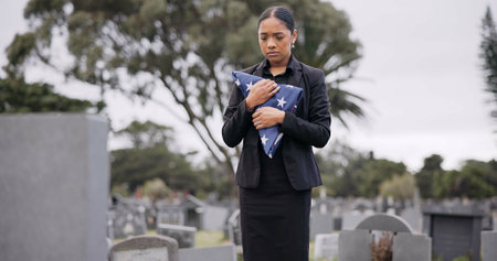 Funeral, death and a sad woman with an american flag at a cemetery in mourning at a memorial service. Sad, usa and an army wife as a widow in a graveyard alone feeling the pain of loss or griefの写真素材