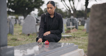 Sad woman, graveyard and rose on tombstone in mourning, loss or grief at funeral or cemetery. Female person with flower in depression, death or goodbye at memorial or burial service for loved oneの写真素材