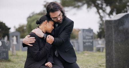 Sad couple, graveyard and hug in loss, grief or mourning together at funeral, tombstone or cemetery....