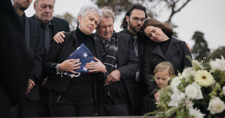 Funeral, cemetery and family with American flag for soldier for respect, ceremony and memorial service. Sad, depression and people by coffin in graveyard mourning military, army and veteran heroの写真素材