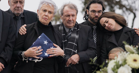 Funeral, cemetery and family with USA flag for veteran for respect, ceremony and memorial service. Remembrance, depression and sad people by coffin in graveyard mourning military, army and soldierの写真素材