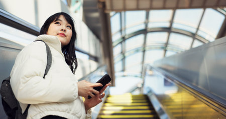 Woman, stairs and smartphone for commute, texting and japanese on social media app. Technology, communication and text message for digital, internet and chatting with backpack, travel and escaltorの写真素材