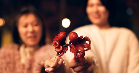 Women, Japan and travel street food at night for octopus delicacy, culture or traditional. Female people, snack and stick for tourism eating experience or cuisine in town for taste, dinner or holidayの写真素材