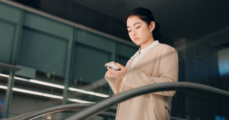 Japanese, escalator and travel with businesswoman, phone or social media with internet, employee or convention. Person, consultant or worker with airport, communication or connection with mobile appの写真素材