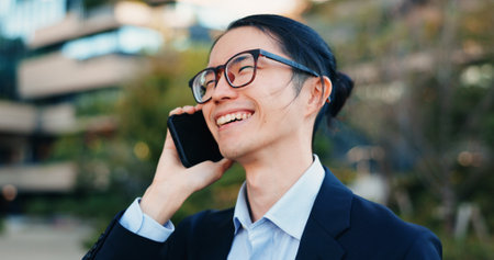 Phone call, city and business man laugh at funny feedback, discussion and chat about news, report or results. Smartphone, humour and happy face of Japanese agent talking with contact on urban commuteの写真素材