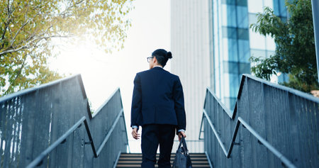 Stairs, walking and back of businessman in the city by office building for travel with career. Outdoor, energy and professional male person commuting on steps to modern workplace in urban town.の写真素材