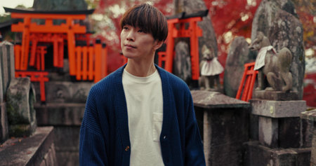 Man, Japanese and outdoor temple for religious zen or adventure, holiday or culture. Male person, fushimi inari shrine and park for religion prayer or traditional experience for peace, god or worshipの写真素材