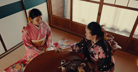 Women with traditional Japanese tea cup, kimono and relax with mindfulness, respect and conversation. Friends at calm tearoom with matcha drink, Asian zen culture and ritual at table for ceremony.の写真素材