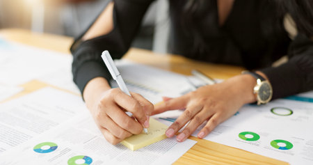 Hands, business person and data analysis, writing on sticky note and paperwork review with graphs...