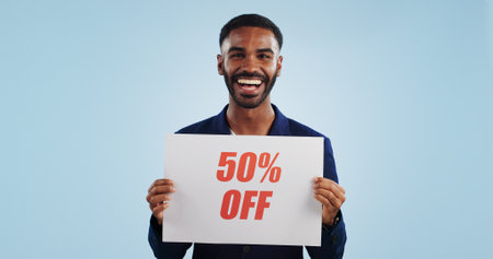 Excited man, portrait and sale sign for advertising, deal or discount against a blue studio background. Happy male person showing billboard or poster for marketing, promotion or special on mockupの写真素材