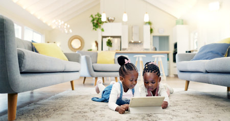 Black girl children on ground with tablet and relax, elearning or watch cartoon movie, sisters at home and screen time. Young female kids, streaming online and subscription to education app or filmの写真素材