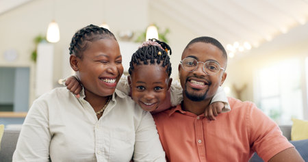 Black family, face and happy with parents and kid at home, love and bonding with hug and spending time together. Man, woman and girl child, happiness and portrait and people smile in living roomの写真素材
