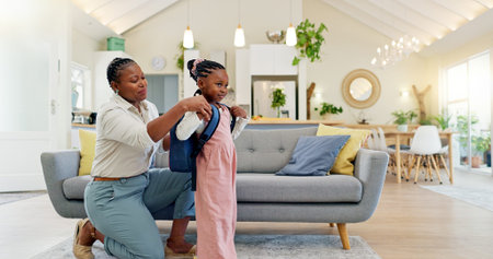 Talking, happy and a mother with a child getting ready for school in the morning. Kiss, laughing and an African mom helping a little girl with a bag in the living room of a house for kindergartenの写真素材