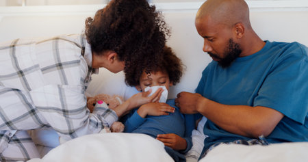 Mother, father and sick child in bed blowing nose for virus, infection or disease in care or support at home. Mom, dad and kid with flu, cold or symptoms for allergies, sinus or morning in bedroomの写真素材