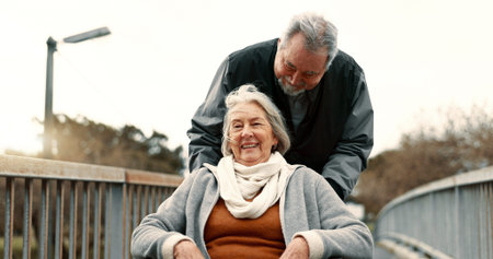 Senior couple, nature and in a wheelchair on a walk for happiness, retirement date or love. Smile, talking and an elderly man and woman with a disability and in a park to relax together in marriageの写真素材