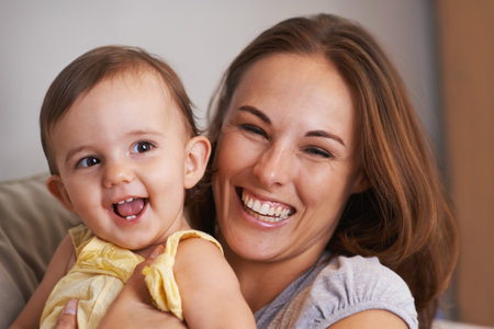 Mother, baby and smile in embrace at home, love and together for bonding in childhood. Mommy, daughter and support for happy toddler in child development, mama and security or connection on sofaの写真素材