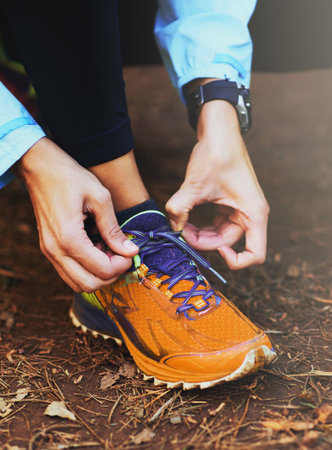 Lacing up. Cropped shot of a woman tying up her running shoes before a trail run.