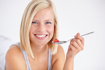Portrait, happy woman and eating fruit salad, healthy diet or nutrition in home bedroom. Face smile, spoon or person with strawberry, hungry for breakfast or organic food for wellness in the morningの写真素材