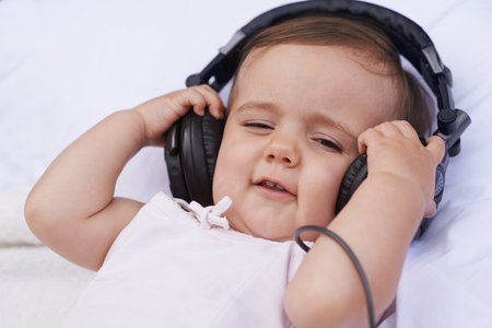 Baby, headphones and listening to music for fun, streaming radio and podcast on bed at home. Child, relax and hearing sound for child development or learning, toddler and calming playlist for audioの写真素材