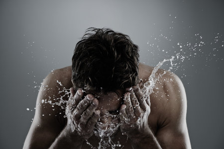 Water, splash and man cleaning face for bathroom routine, cleanse or fresh skincare in morning beauty treatment. Studio, skin hydration and model facial wash, hygiene and grooming on grey backgroundの写真素材