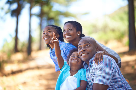 Happy family, children and pointing in forest for bonding, adventure or outdoor holiday in nature. African mother, father and kids smile for fun day in support, love or weekend exploring in the woodsの写真素材