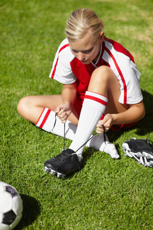 Girl, soccer and tie shoelace on field, safety and start training for fitness, health or competition on pitch. Person, shoes and football for preparation, ready or game for sport contest on grassの写真素材