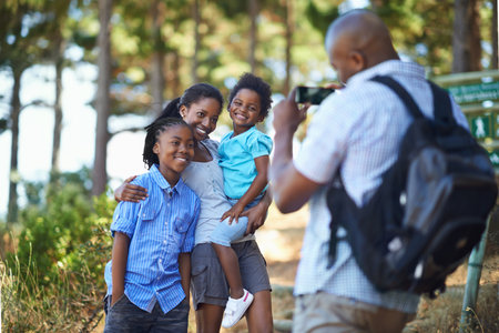 Smile, photograph and a black family hiking in the forest together for travel, tourism or adventure. Love, photography or memory with a man, woman and children in the woods or wilderness for freedomの写真素材