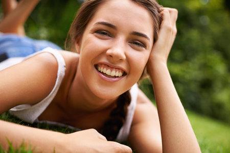 Woman, portrait and laughing on grass for relax with sunshine, enjoyment or weekend break in summer. Young person, funny and confident on lawn, garden or backyard of home for fresh air in environmentの写真素材