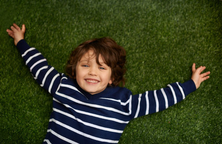 Happy, above and portrait of child on grass for relax, playful fun and happiness in garden. Family, nature and young boy for childhood, playing and freedom on weekend, vacation or holiday outdoorsの写真素材