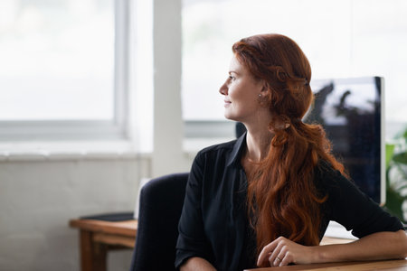 Woman, office and think with vision at window for company idea, growth and hope with future in startup business. Female person, entrepreneur and desk with computer at work as hr for corporate.の写真素材