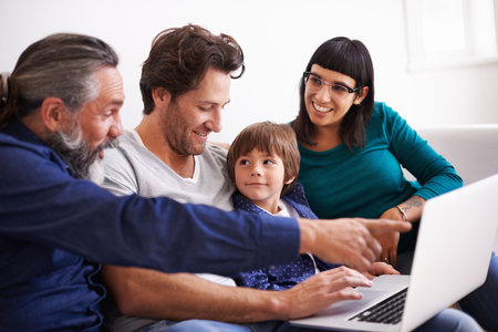 Family, laptop and learning or streaming on sofa, smile and bonding in living room. Video call, internet and chat with grandfather pointing, parents and young boy for communication online in homeの写真素材