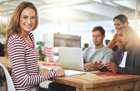 Portrait, meeting and smile of business woman at table in startup, office or company for creative career. Face, coworking and happy professional entrepreneur at desk, employee or copywriter with teamの写真素材