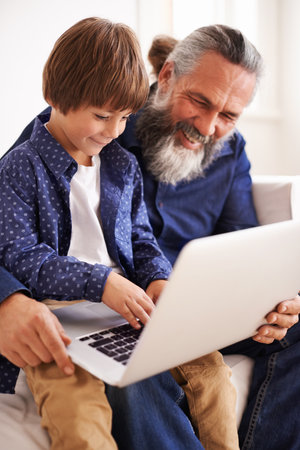 Grandfather, laptop and boy child for streaming, elearning and bonding in living room. Focus, family and internet for play and son typing, childhood development and games or technology for learningの写真素材
