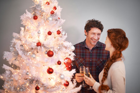 Couple, Christmas and tree with champagne for celebration together for festive season or holiday vacation, decoration or lights. Man, woman and drinking alcohol in home or happy event, love or giftsの写真素材
