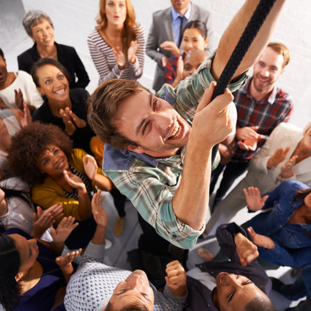 Business people, smile and man climbing rope for goals, target or achievement with team support. High angle, diversity and happy professional person with group of colleagues for ambition in office.の写真素材