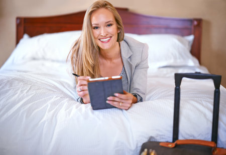 Business woman, tablet and portrait in hotel room with travel suitcase, luggage and planning for work conference. Technology, bed and hospitality with smile and networking of a professional on a tripの写真素材