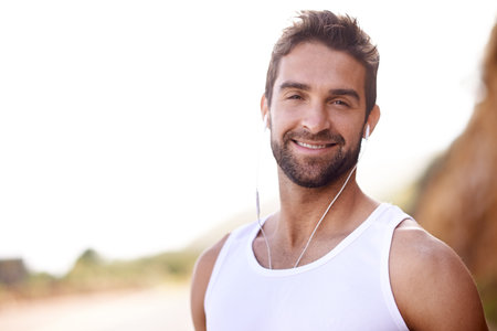 Fitness, headphones and portrait of man in nature for exercise, workout and music for training. Male person, earphones and mockup with smile for streaming, audio or podcast for outdoor morning cardioの写真素材