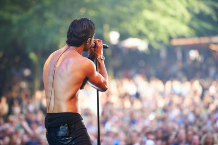 Singer, man and performance at music concert, festival or party with crowd of people. Rock, celebration and musician on stage for show, talent or back of artist on microphone outdoor for social eventの写真素材