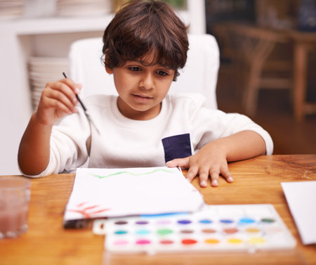 Little boy, painting and drawing with brush on paper for art, design or creativity with color at home. Young child or kid with smile and paintbrush for colorful palette, artwork or artistic skillsの写真素材